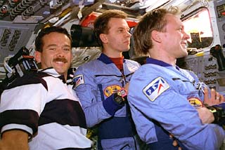 Avdeyev, Gidzenko, Hadfield in flight deck looking at Mir through shuttle windows